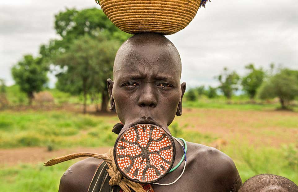 African woman with lip disk holding a traditional tribal bowl